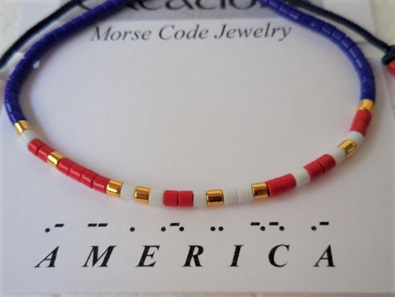 May include: A red, white, and blue beaded bracelet with gold accents. The bracelet spells out "AMERICA" in Morse code.