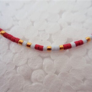May include: A close-up of a red, white, and blue beaded necklace with gold accents. The beads are small and round, and the necklace is strung on a thin cord.