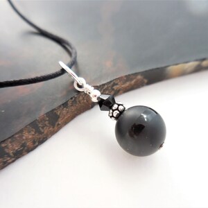 May include: A black onyx bead necklace with a silver clasp and a black crystal bead. The necklace is on a black cord.