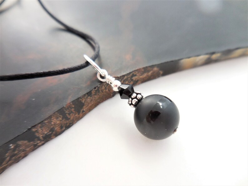 May include: A black onyx bead necklace with a silver clasp and a black crystal bead. The necklace is on a black cord.