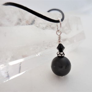 May include: A black onyx bead necklace with a silver clasp and a black crystal accent. The necklace is on a black cord.