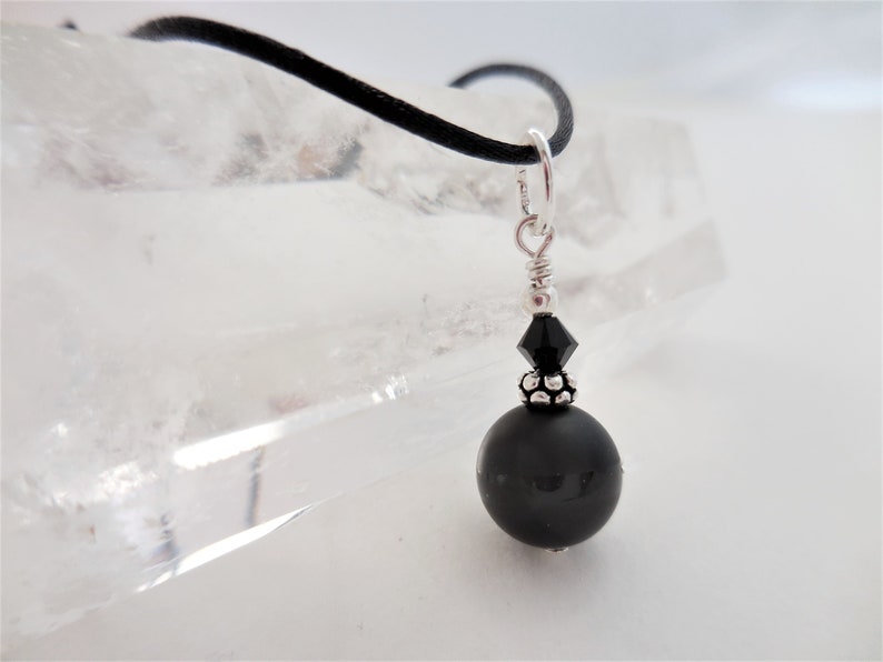 May include: A black onyx bead necklace with a silver clasp and a black crystal accent. The necklace is on a black cord.