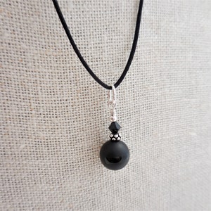 May include: A black onyx pendant necklace with a black crystal bead and a silver chain. The necklace is on a black cord.