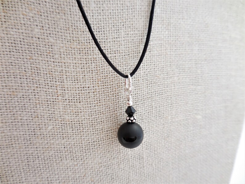 May include: A black onyx pendant necklace with a black crystal bead and a silver chain. The necklace is on a black cord.