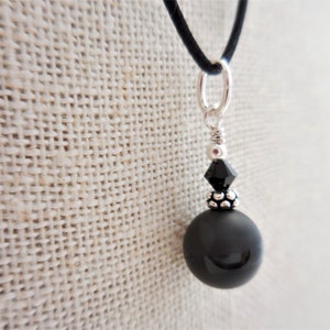 May include: A black onyx pendant necklace with a silver chain and a black crystal accent. The pendant is round and has a smooth, polished finish.