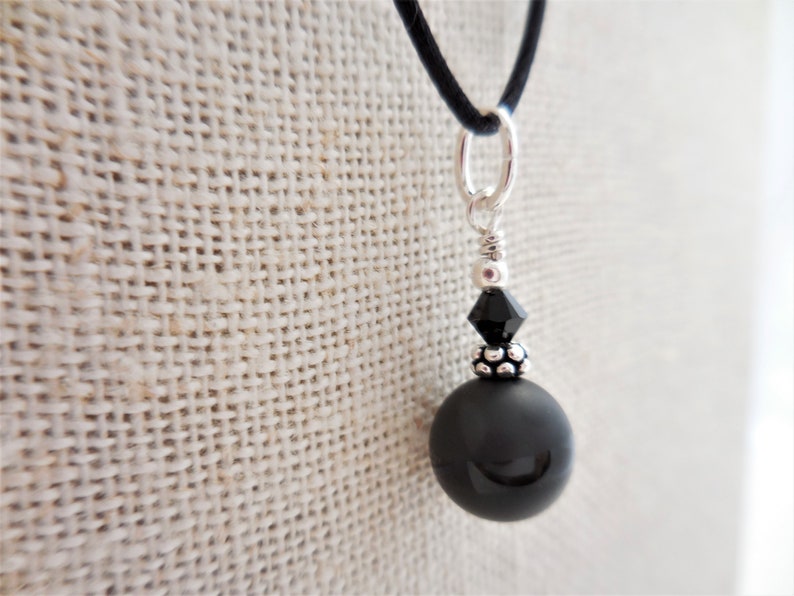 May include: A black onyx pendant necklace with a silver chain and a black crystal accent. The pendant is round and has a smooth, polished finish.