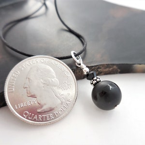 May include: A black onyx bead necklace with a silver pendant and a black crystal bead. The necklace is on a black cord and is about the size of a quarter.