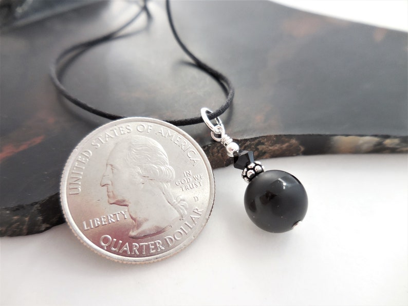 May include: A black onyx bead necklace with a silver pendant and a black crystal bead. The necklace is on a black cord and is about the size of a quarter.
