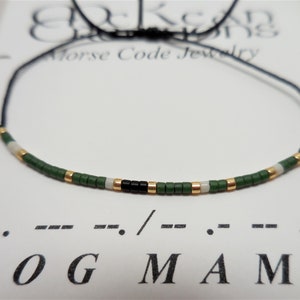 May include: A green, white, black, and gold beaded bracelet on a black cord. The bracelet spells out "DOG MAMA" in Morse code.