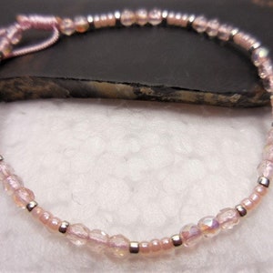 Puede incluir: Un delicado brazalete de cuentas rosas y plateadas con un cierre simple de nudo.