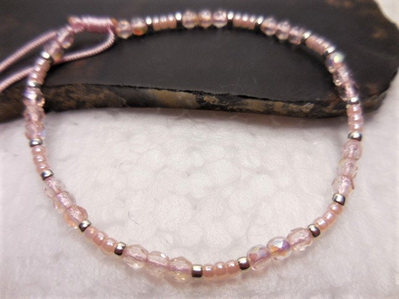 Puede incluir: Un delicado brazalete de cuentas rosas y plateadas con un cierre simple de nudo.