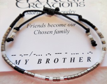 May include: A black and white beaded bracelet with a black cord and a silver toggle clasp. The bracelet spells out "MY BROTHER" in Morse code.