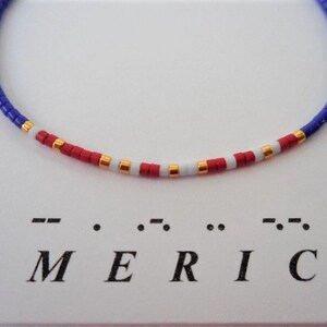 May include: A blue, red, white, and gold beaded bracelet with the word "AMERICA" spelled out in braille below it.