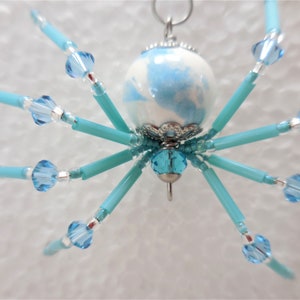 Puede incluir: Un adorno de ara&ntilde;a de cuentas azules y blancas con un lazo plateado para colgar.