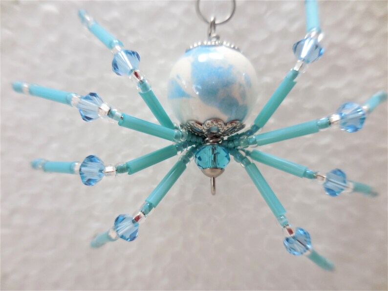 Puede incluir: Un adorno de ara&ntilde;a de cuentas azules y blancas con un lazo plateado para colgar.