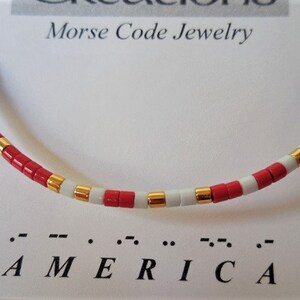 May include: A red, white, and blue beaded bracelet with gold accents. The bracelet spells out "AMERICA" in Morse code.