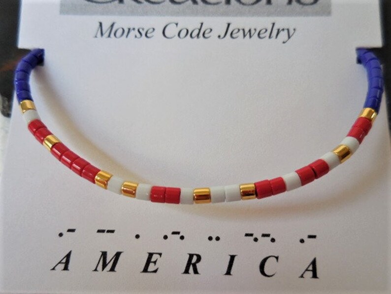 May include: A red, white, and blue beaded bracelet with gold accents. The bracelet spells out "AMERICA" in Morse code.