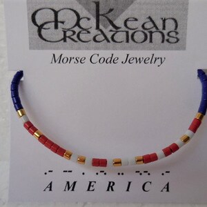 May include: A red, white, and blue beaded bracelet with gold accents. The bracelet spells out "AMERICA" in Morse code.
