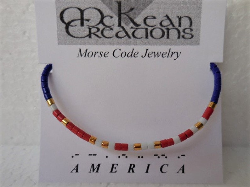 May include: A red, white, and blue beaded bracelet with gold accents. The bracelet spells out "AMERICA" in Morse code.