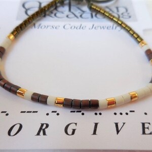 May include: A brown, white, and gold beaded bracelet with the word "FORGIVEN" spelled out in Morse code below.