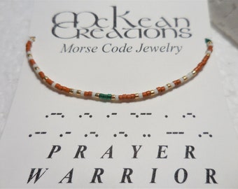 May include: A brown, white, and green beaded bracelet with the word "PRAYER WARRIOR" spelled out in Morse code.
