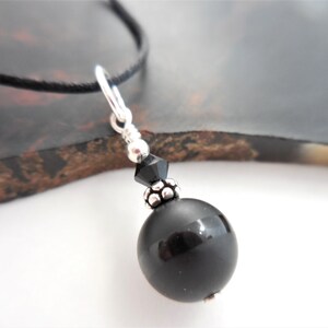 May include: A black onyx bead necklace with a silver clasp and a black crystal accent. The necklace is on a black cord.