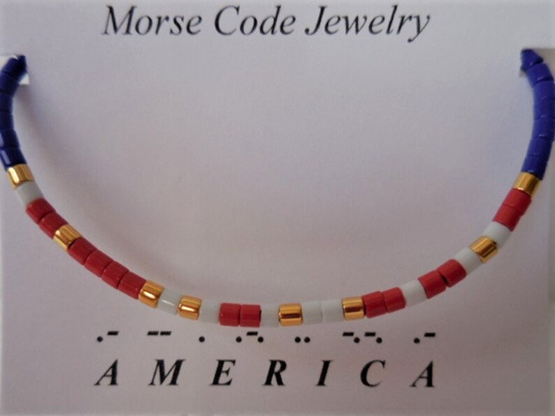 May include: A red, white, and blue beaded bracelet with gold accents. The bracelet spells out "AMERICA" in Morse code.