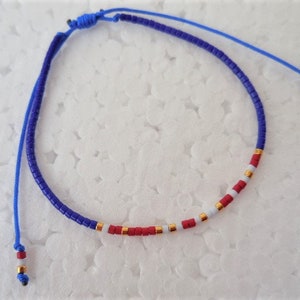 May include: A blue and white beaded bracelet with red accents. The bracelet is made with small, round beads and has a simple knot closure.