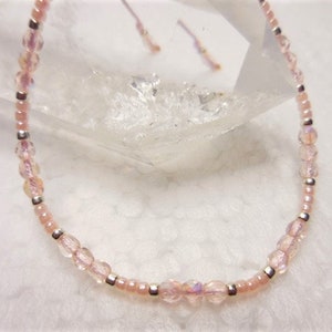 Puede incluir: Un delicado brazalete de cuentas rosas y plateadas con cierre de nudo deslizante. Las cuentas son iridiscentes y tienen un brillo sutil.
