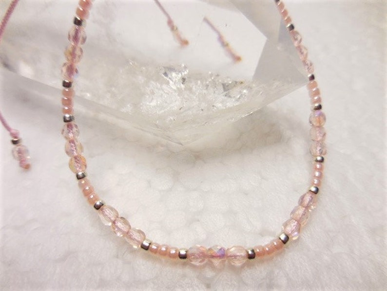 Puede incluir: Un delicado brazalete de cuentas rosas y plateadas con cierre de nudo deslizante. Las cuentas son iridiscentes y tienen un brillo sutil.