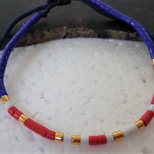 May include: A blue, white, and red beaded bracelet with gold accents. The bracelet is made of small, round beads and has a simple, elegant design.