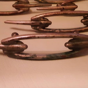 Może przedstawiać: Zestaw pięciu antycznych metalowych gałek do szuflad o unikalnym wzorze z podwójną pętlą i spiczastym końcem. Gałki są w kolorze srebrnym z efektem zużycia.