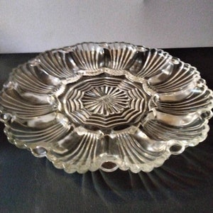 May include: A clear glass serving dish with a scalloped edge and a central, starburst-patterned section. The dish has a raised, circular base.