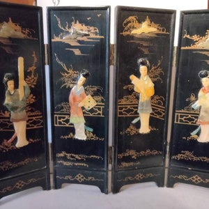 May include: A four-panel black folding screen with gold accents and painted scenes of Asian women in traditional clothing. Each panel features a different woman with a unique design and color scheme.
