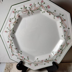 May include: White octagonal dinner plate with a green and white border. The plate has a floral design with pink flowers and green vines with pink ribbons.