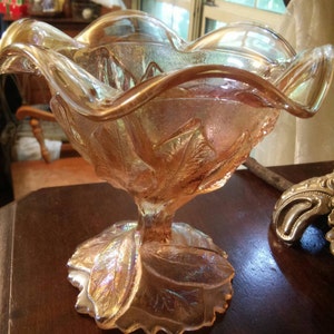 May include: A vintage iridescent glass candy dish with a ruffled rim and a leaf design. The dish is made of clear glass with a pink and gold iridescent finish.