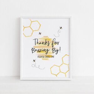 May include: White framed sign with a yellow and orange watercolor background. The sign says "Thanks for Buzzing By! Please take one." with a honeycomb pattern and bee illustrations.