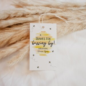 May include: A white thank you tag with a yellow and orange watercolor background. The tag says "Thanks for buzzing by!" with the text "Lots of love, Eleanor Agnes" below. There are small black and yellow bee illustrations around the text.