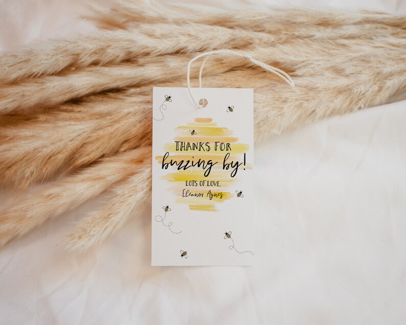 May include: A white thank you tag with a yellow and orange watercolor background. The tag says "Thanks for buzzing by!" with the text "Lots of love, Eleanor Agnes" below. There are small black and yellow bee illustrations around the text.