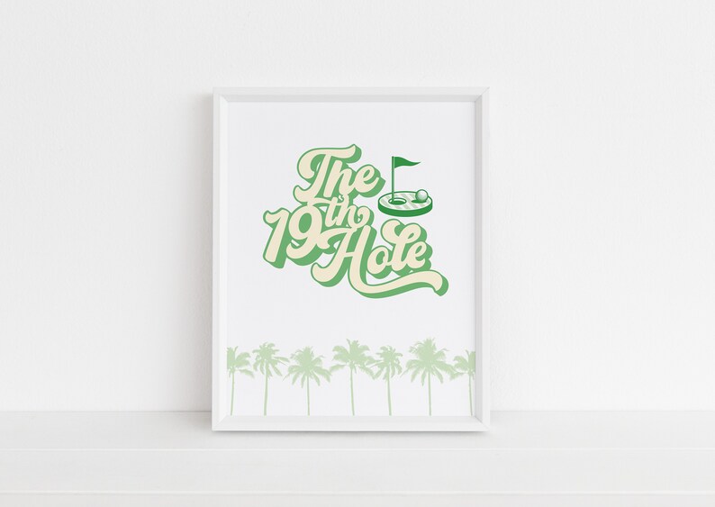 May include: A white framed print with green text that reads "The 19th Hole" with a green golf hole and flag illustration. The bottom of the print has a row of green palm trees.