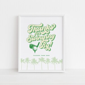 May include: A white framed print with green text that says "Thanks for Swinging By!" with a golf club and ball graphic. The text "Please Take One" is below the graphic. There are green palm trees at the bottom of the print.