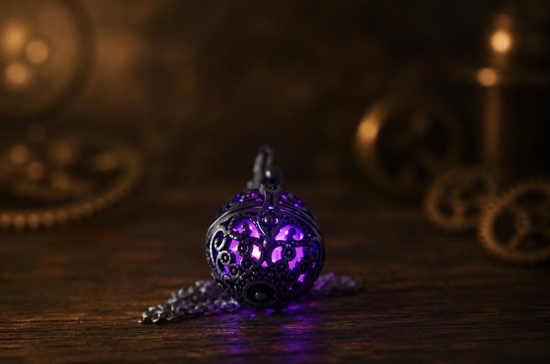 May include: A spherical metal pendant featuring an intricate, dark-toned filigree cage design. The interior of the pendant emits a vibrant, glowing purple light that shines through the decorative cutouts. A matching metal chain is attached to the top.