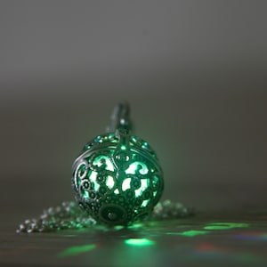May include: A silver pendant necklace with a round, openwork design. The pendant is glowing green from within.