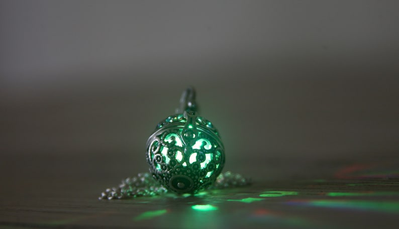 May include: A silver pendant necklace with a round, openwork design. The pendant is glowing green from within.