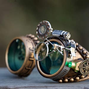 May include: Steampunk goggles with brass and copper accents, featuring a magnifying glass, a compass, and a green LED light. The goggles have a black elastic strap.