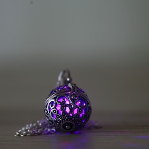 May include: A silver pendant with a delicate, intricate design. The pendant is hollow and glows with a vibrant purple light.