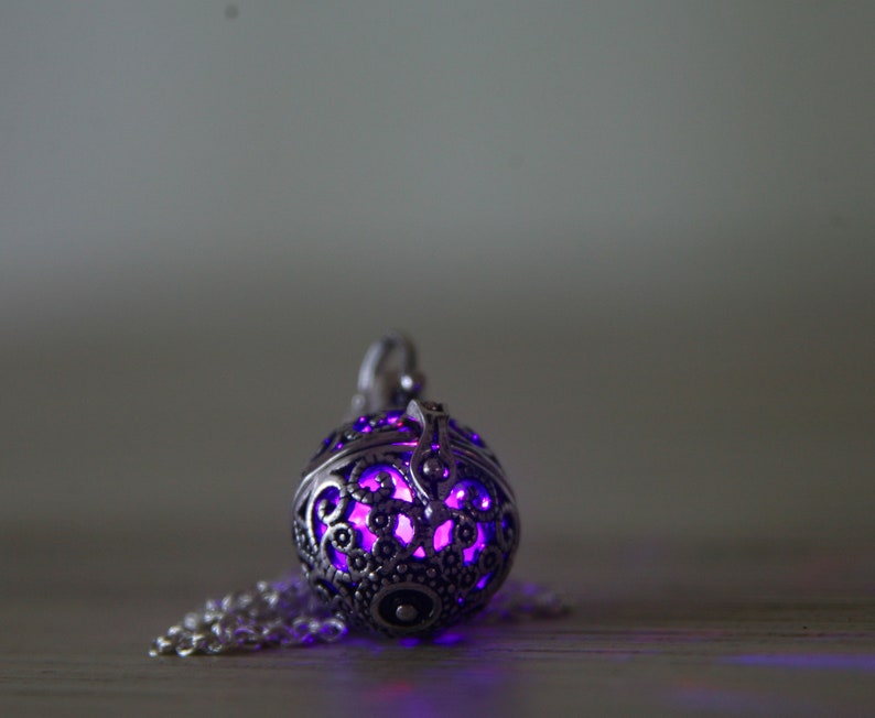 May include: A silver pendant with a delicate, intricate design. The pendant is hollow and glows with a vibrant purple light.