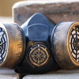May include: A black gas mask with gold-colored filters and a compass design on the front.