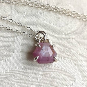May include: A silver chain necklace with a pink gemstone pendant. The pendant is a faceted, irregular shape with silver accents.