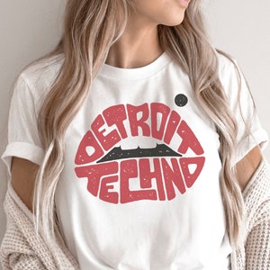 May include: White t-shirt with a red lip design that says "Detroit Techno" in black text.